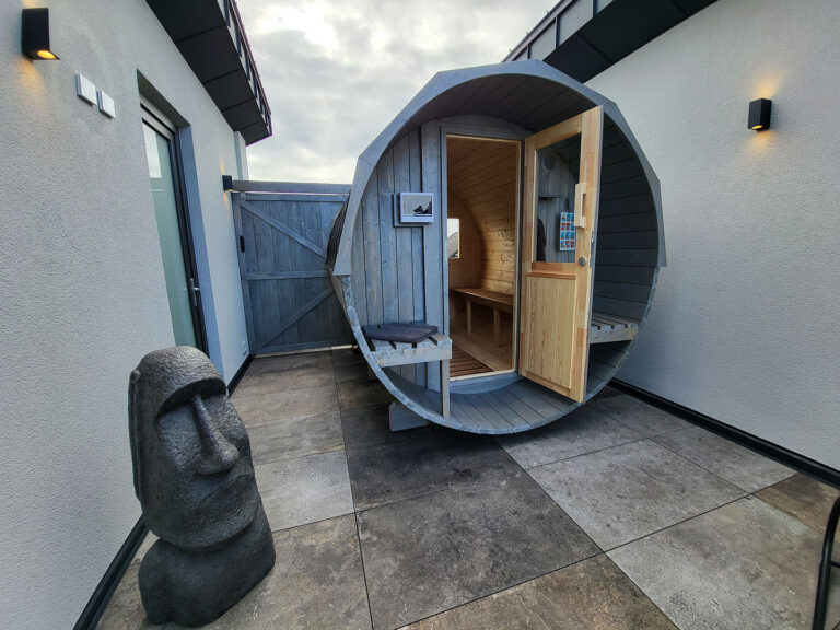 Private Außensauna im Fass-Design auf der Dachterrasse eines modernen Ferienhauses, neben einer stilvollen Steinskulptur.