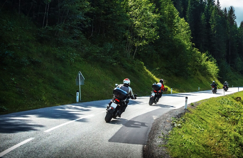 Motorradfahrer fahren in einer Gruppe auf einer kurvigen Straße durch einen grünen Wald.